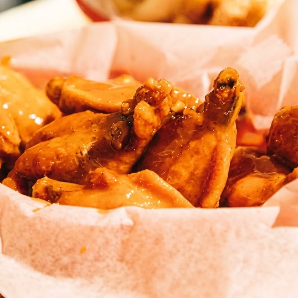 Close-up of a basket of golden-brown chicken wings coated in a glossy sauce, lined with white paper.