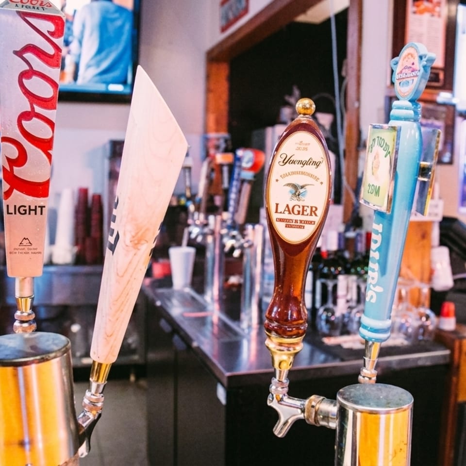 Beer taps with Coors Light, Yuengling Lager, and other brands at a bar with patrons.
