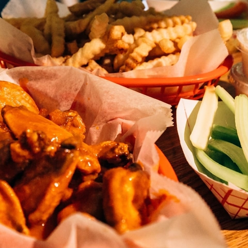 Baskets of buffalo wings, crinkle-cut fries, celery sticks, and dipping sauces on a wooden table.