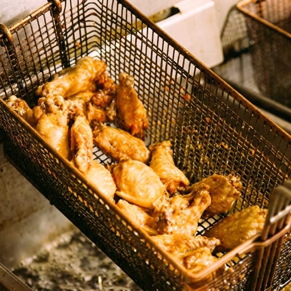 Golden-brown chicken wings frying in a metal basket, submerged in hot oil in a deep fryer.