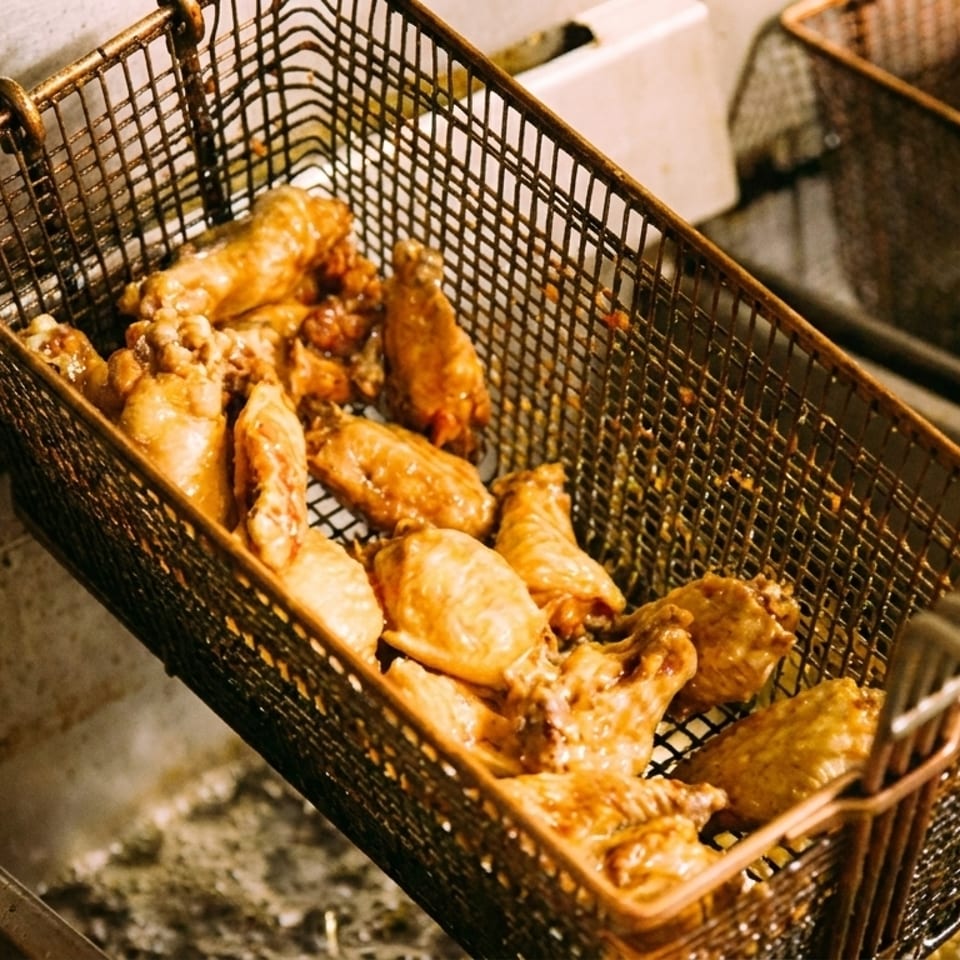 Golden-brown chicken wings frying in a metal basket, submerged in hot oil in a deep fryer.